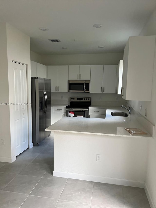 kitchen featuring appliances with stainless steel finishes, sink, white cabinets, light tile patterned floors, and kitchen peninsula