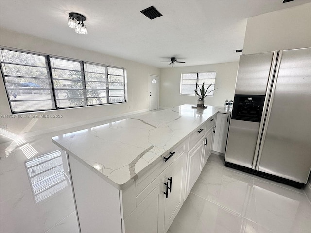 kitchen with kitchen peninsula, white cabinetry, ceiling fan, light stone counters, and stainless steel refrigerator with ice dispenser