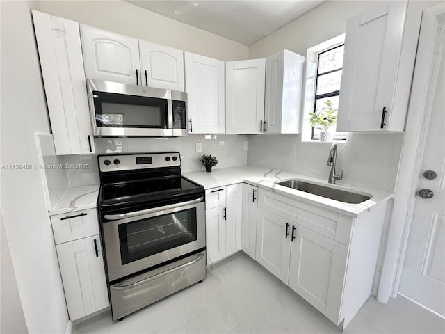 kitchen with sink, light stone counters, white cabinets, stainless steel appliances, and backsplash