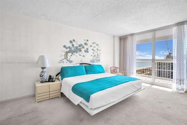 carpeted bedroom with a water view, expansive windows, a textured ceiling, and access to outside