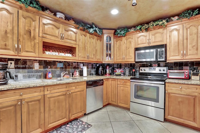 kitchen featuring light stone counters, sink, light tile patterned floors, and appliances with stainless steel finishes