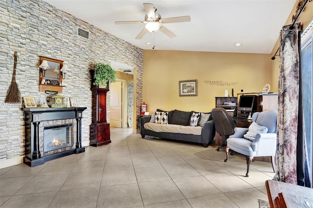 living room featuring light tile patterned floors, a stone fireplace, and ceiling fan