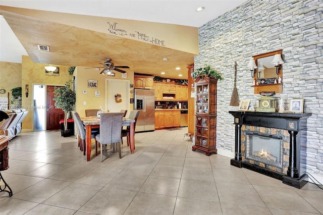 dining space featuring light tile patterned floors, a stone fireplace, ceiling fan, and a high ceiling