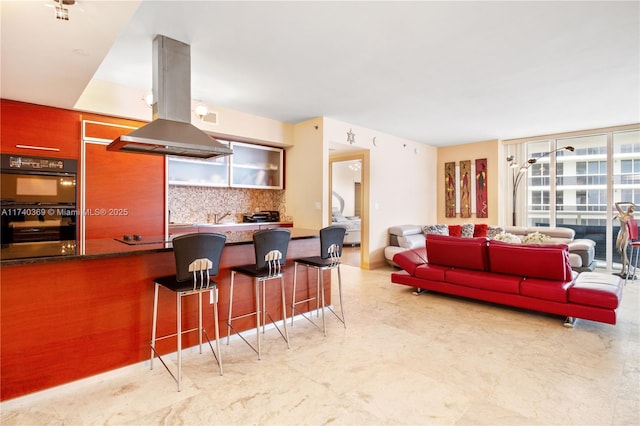 kitchen with island range hood, black double oven, decorative backsplash, and a breakfast bar