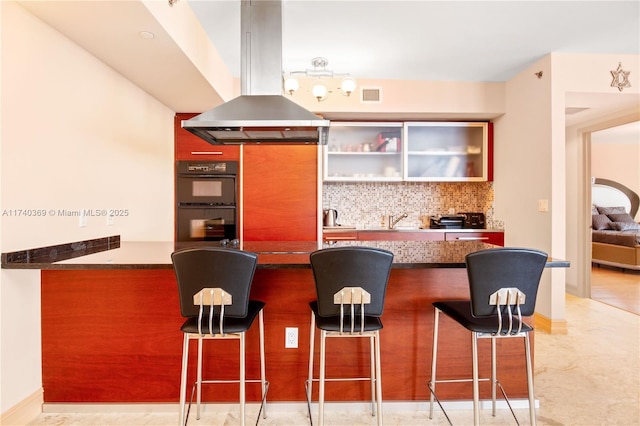 kitchen with a breakfast bar, island range hood, sink, black double oven, and kitchen peninsula