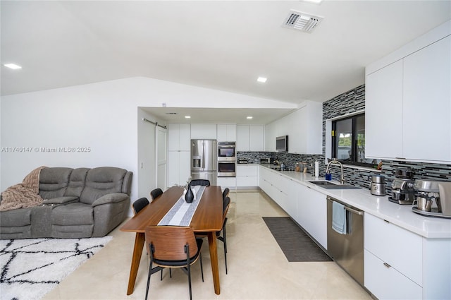 kitchen featuring appliances with stainless steel finishes, white cabinetry, lofted ceiling, decorative backsplash, and a barn door