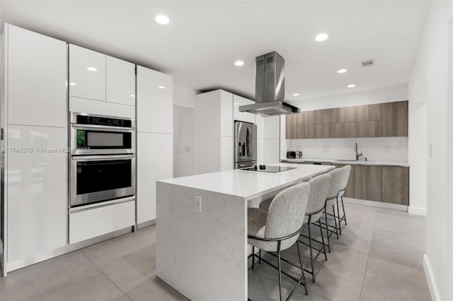 kitchen with white cabinetry, island exhaust hood, appliances with stainless steel finishes, and a kitchen island