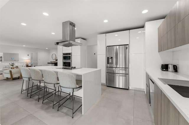 kitchen featuring white cabinetry, stainless steel appliances, a center island, a kitchen breakfast bar, and island exhaust hood