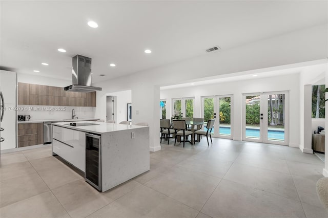 kitchen with french doors, island range hood, an island with sink, beverage cooler, and white cabinets