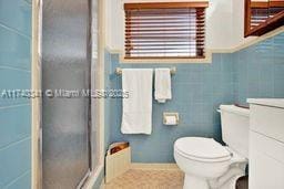 bathroom featuring walk in shower, vanity, toilet, and tile walls