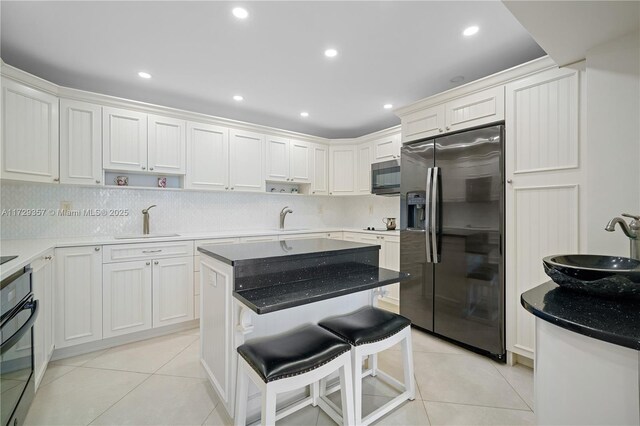 kitchen with sink, appliances with stainless steel finishes, white cabinets, a kitchen island, and light tile patterned flooring