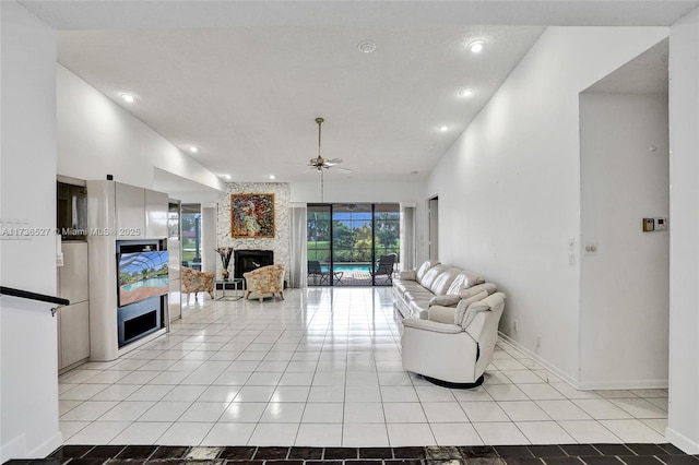 living area featuring light tile patterned floors, a ceiling fan, a stone fireplace, high vaulted ceiling, and baseboards