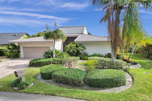 view of front of property featuring decorative driveway, a tile roof, stucco siding, an attached garage, and a front yard