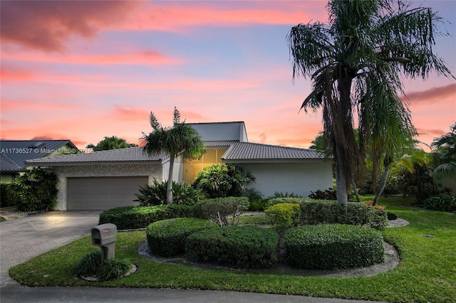 view of front of home featuring driveway, a lawn, a tiled roof, an attached garage, and stucco siding