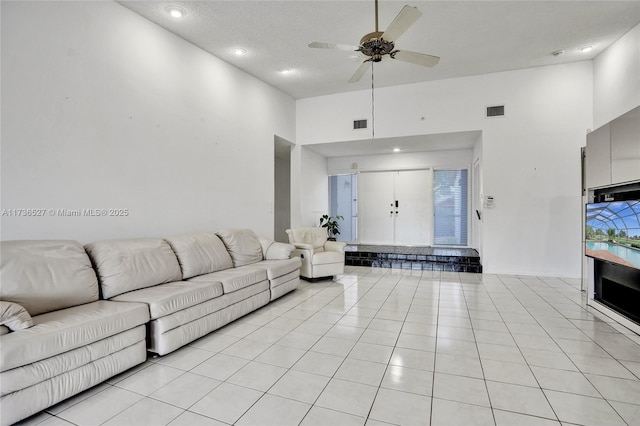 living room featuring light tile patterned floors, ceiling fan, a high ceiling, and visible vents