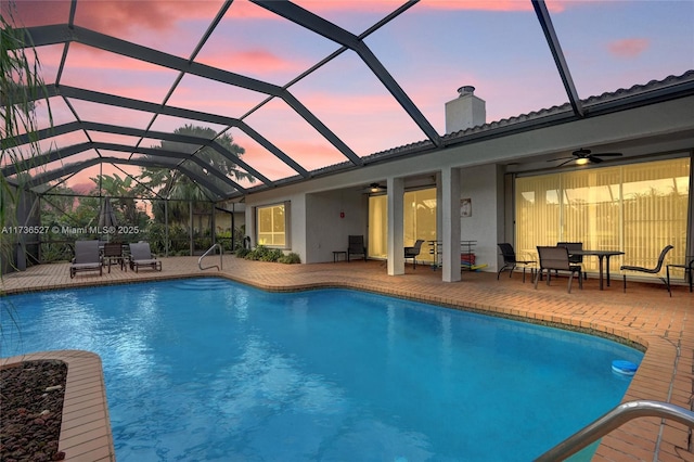 outdoor pool with glass enclosure, a patio area, and ceiling fan