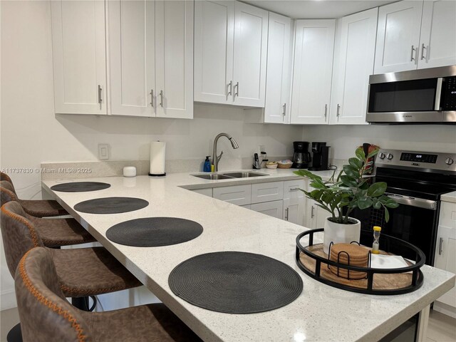 kitchen with sink, a breakfast bar area, stainless steel appliances, and white cabinets