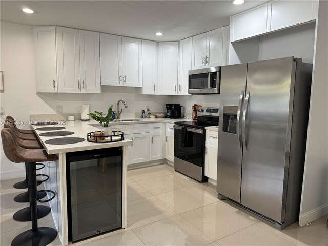 kitchen with appliances with stainless steel finishes, white cabinetry, sink, beverage cooler, and a kitchen breakfast bar