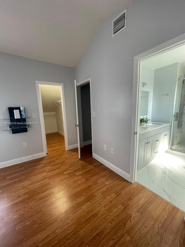 unfurnished bedroom with hardwood / wood-style flooring, a walk in closet, connected bathroom, and vaulted ceiling