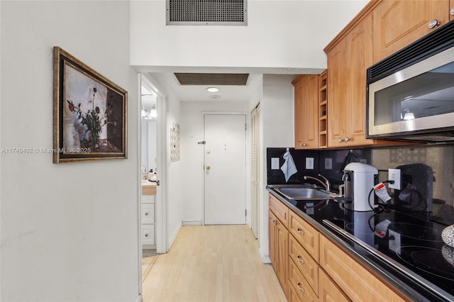 kitchen featuring black electric cooktop, sink, backsplash, and light wood-type flooring