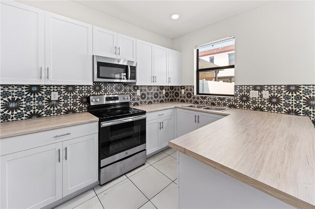 kitchen with light tile patterned flooring, appliances with stainless steel finishes, tasteful backsplash, white cabinetry, and sink