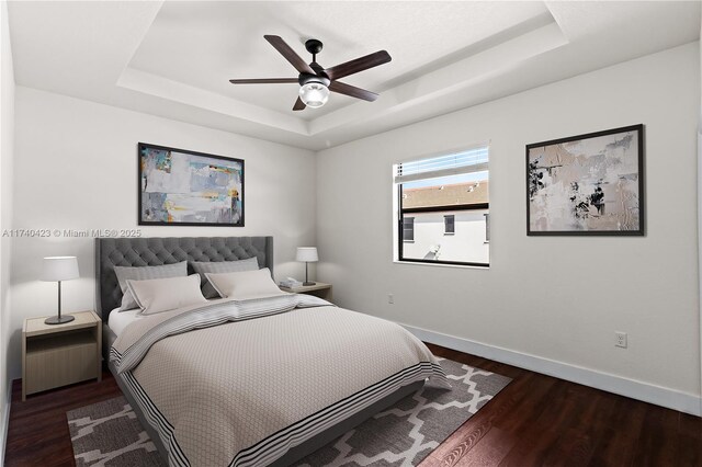 bedroom with dark wood-type flooring, a raised ceiling, and ceiling fan