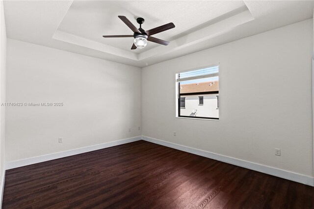 spare room featuring dark wood-type flooring, ceiling fan, and a raised ceiling