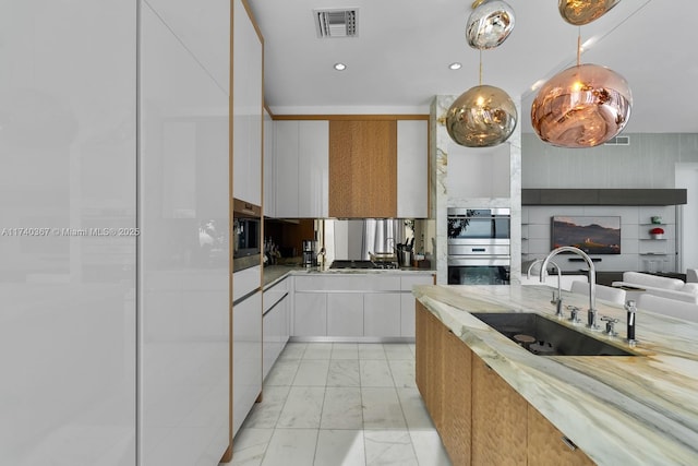 kitchen featuring pendant lighting, a fireplace, white cabinetry, sink, and stainless steel appliances