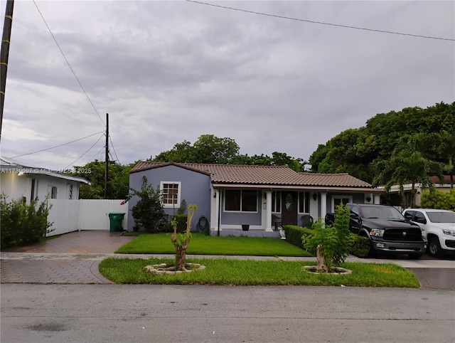 view of front of property with a tile roof, fence, decorative driveway, a front yard, and stucco siding