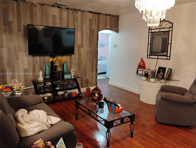 living room with an inviting chandelier, dark hardwood / wood-style flooring, and wood walls