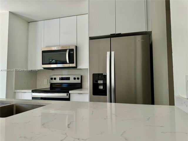 kitchen with white cabinetry, stainless steel appliances, light stone countertops, and decorative backsplash