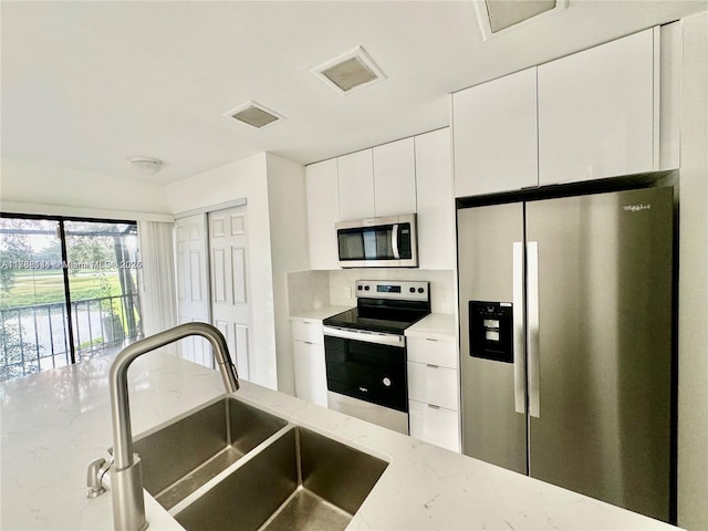 kitchen with appliances with stainless steel finishes, sink, white cabinets, and light stone counters