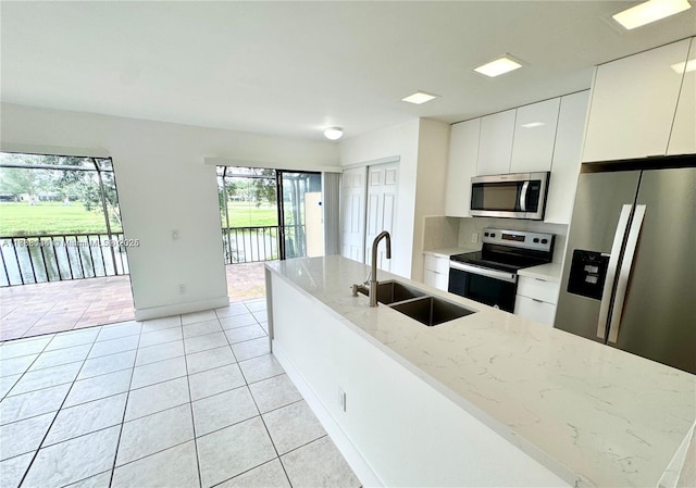 kitchen featuring appliances with stainless steel finishes, sink, white cabinets, light tile patterned floors, and light stone counters