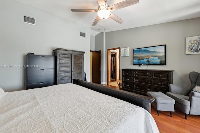 bedroom with vaulted ceiling, a walk in closet, ceiling fan, and light wood-type flooring