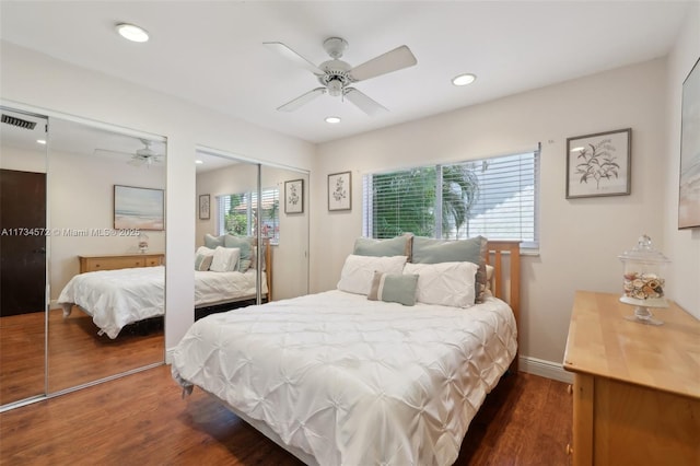 bedroom with dark wood-type flooring, ceiling fan, and two closets