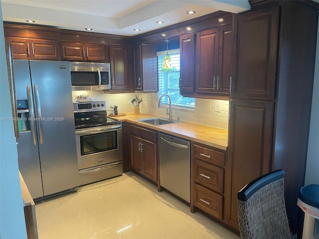 kitchen with sink, wooden counters, hanging light fixtures, appliances with stainless steel finishes, and decorative backsplash