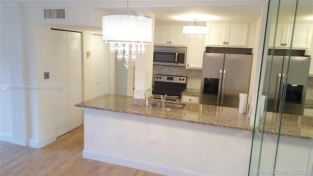 kitchen featuring appliances with stainless steel finishes, hanging light fixtures, white cabinets, stone counters, and backsplash