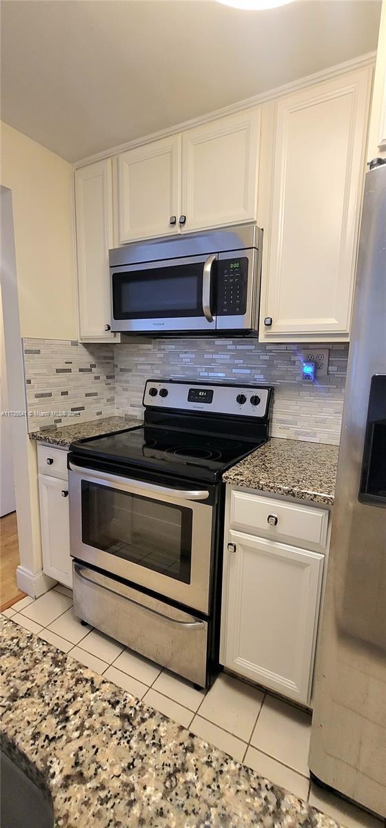 kitchen with appliances with stainless steel finishes, white cabinetry, and light stone counters