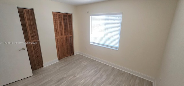 unfurnished bedroom featuring light hardwood / wood-style floors and multiple closets