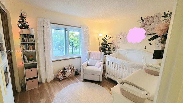 bedroom featuring a crib, wood-type flooring, and a textured ceiling