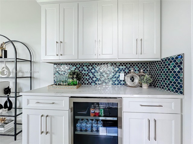 bar featuring wine cooler, backsplash, light stone counters, and white cabinets