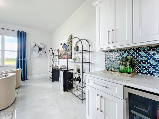 kitchen featuring tasteful backsplash, light stone countertops, white cabinets, vaulted ceiling, and beverage cooler