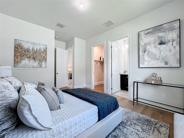 bedroom with a closet, a walk in closet, connected bathroom, and light hardwood / wood-style flooring