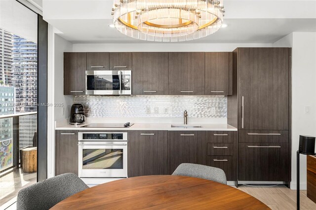 kitchen with appliances with stainless steel finishes, sink, backsplash, dark brown cabinetry, and light hardwood / wood-style flooring