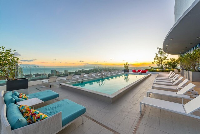 pool at dusk featuring a patio and a water view