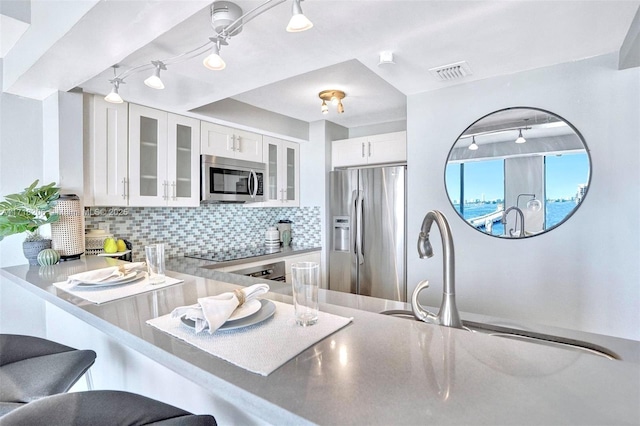 kitchen featuring appliances with stainless steel finishes, backsplash, white cabinets, a kitchen bar, and kitchen peninsula