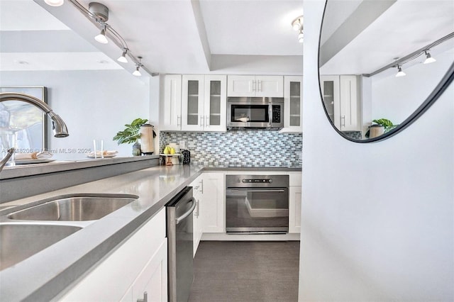 kitchen featuring rail lighting, sink, white cabinetry, stainless steel appliances, and decorative backsplash