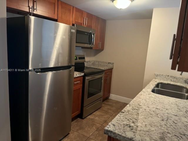 kitchen featuring light stone counters, sink, light tile patterned floors, and stainless steel appliances