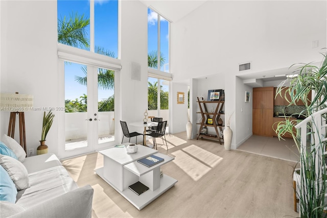 living room featuring french doors, a towering ceiling, and light hardwood / wood-style floors