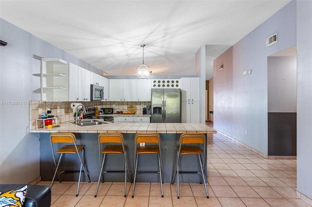 kitchen with kitchen peninsula, a breakfast bar, appliances with stainless steel finishes, white cabinets, and pendant lighting